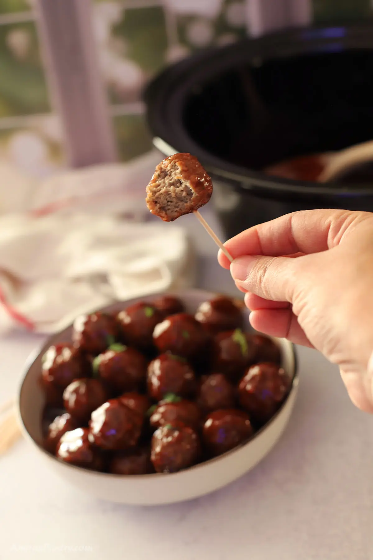 BBQ meatballs on a plaåA hand holding one meatball with a toothpick.