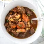 A big bowl of beef stew with a spoon in it.