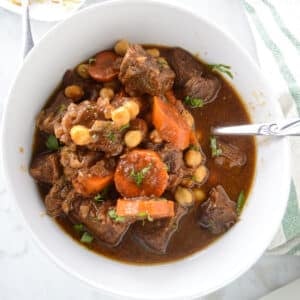 A big bowl of beef stew with a spoon in it.