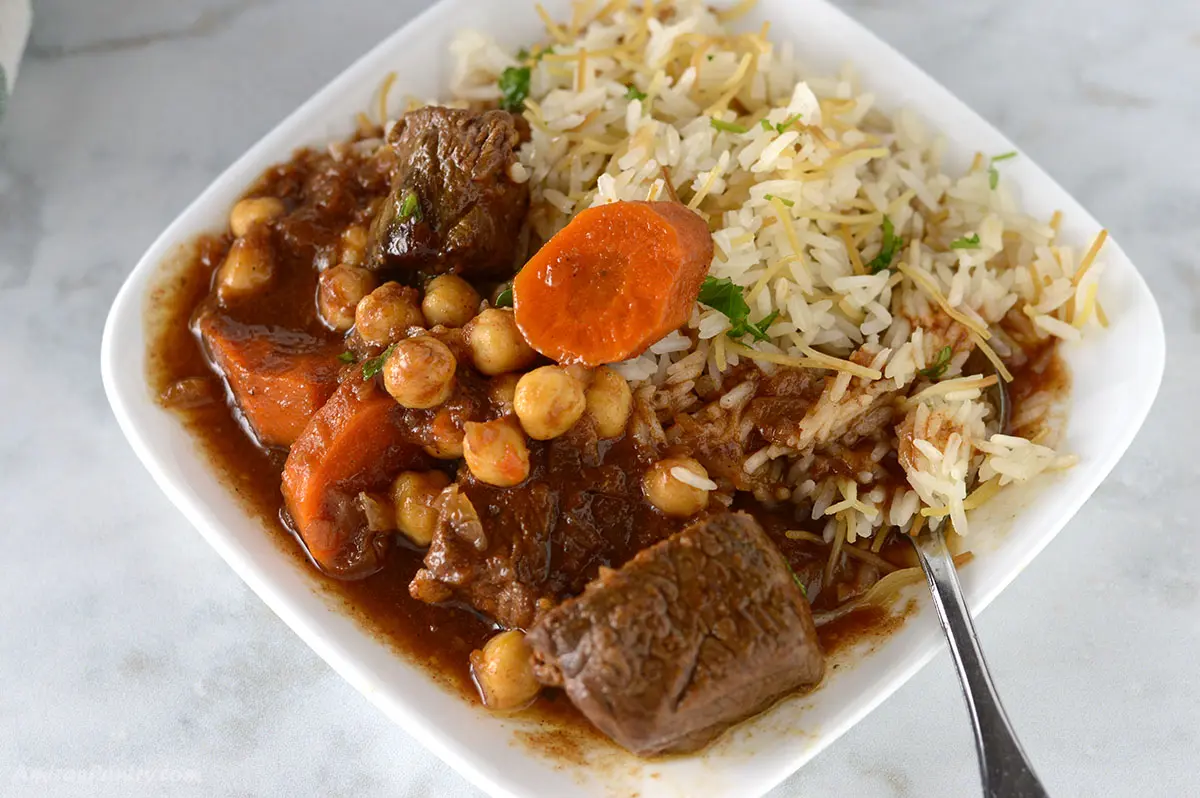 Beef stew on a white plate with rice.