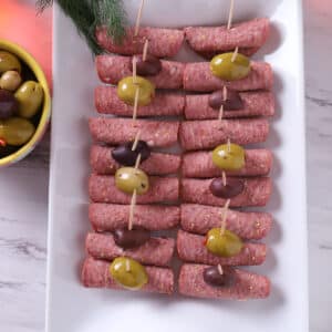 A top view os a white tray with salami roll ups.