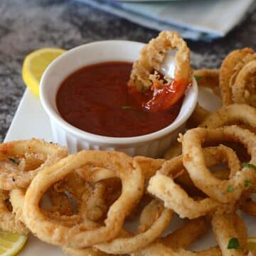 Frid calamari rings on a white plate with one dipped in sauce.