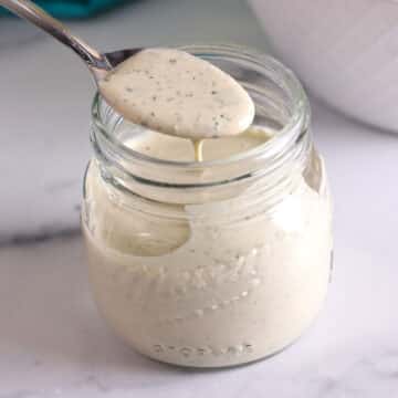 A spoon scooping some tahini sauce from a jar.