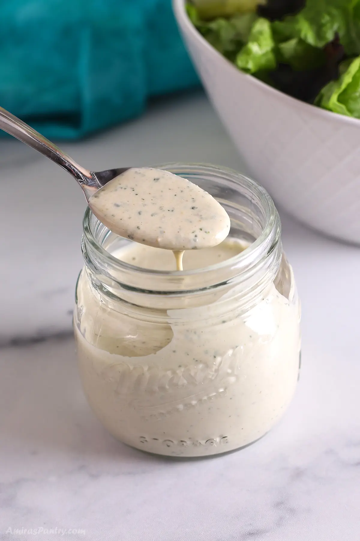 A spoon scooping some lemon herb tahini out of a jar.