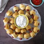 A top view of little smokies with crescent rolls placed on a white serving plate.