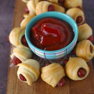Lil smokies wrapped in crescent rolls on a board with dips.