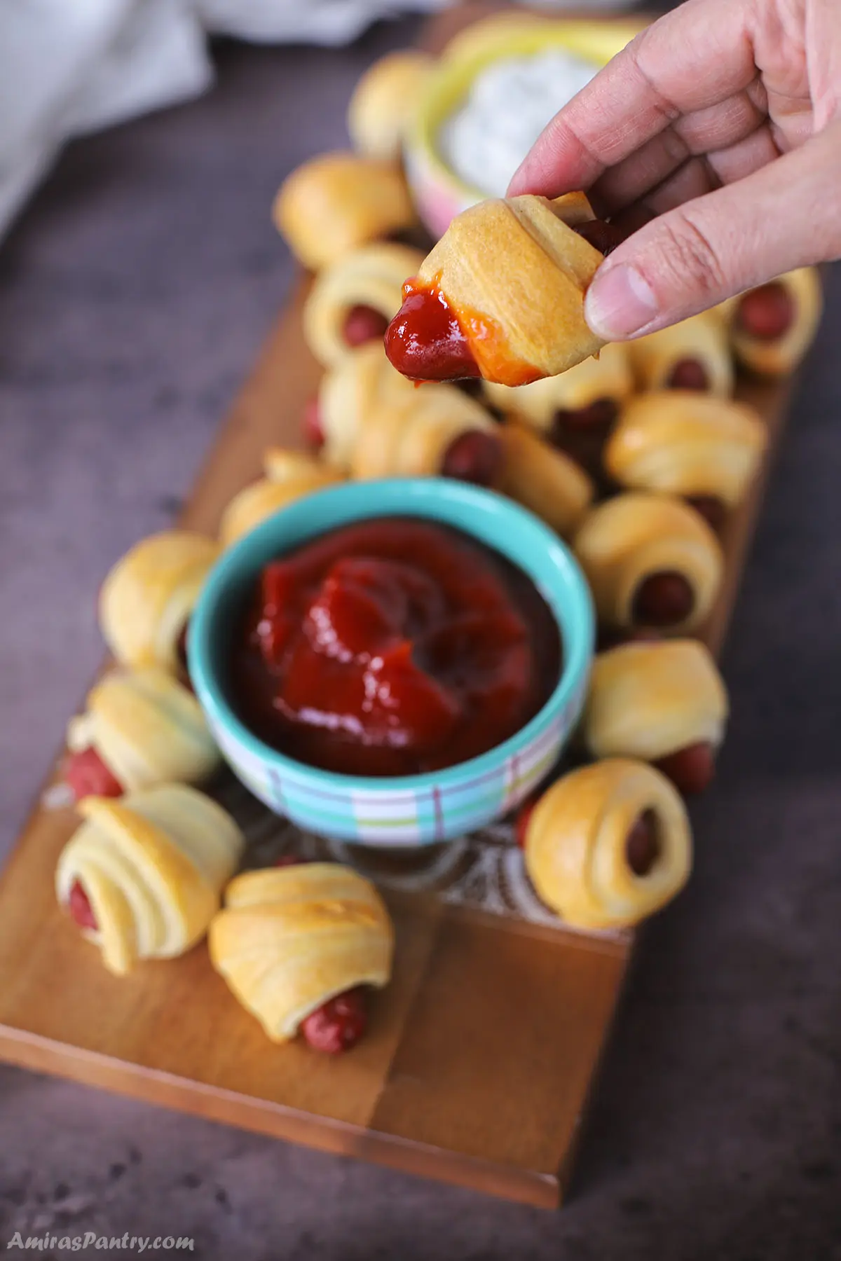 A hang holding onw lilt smokies with crescent rolls dipped in ketchup.