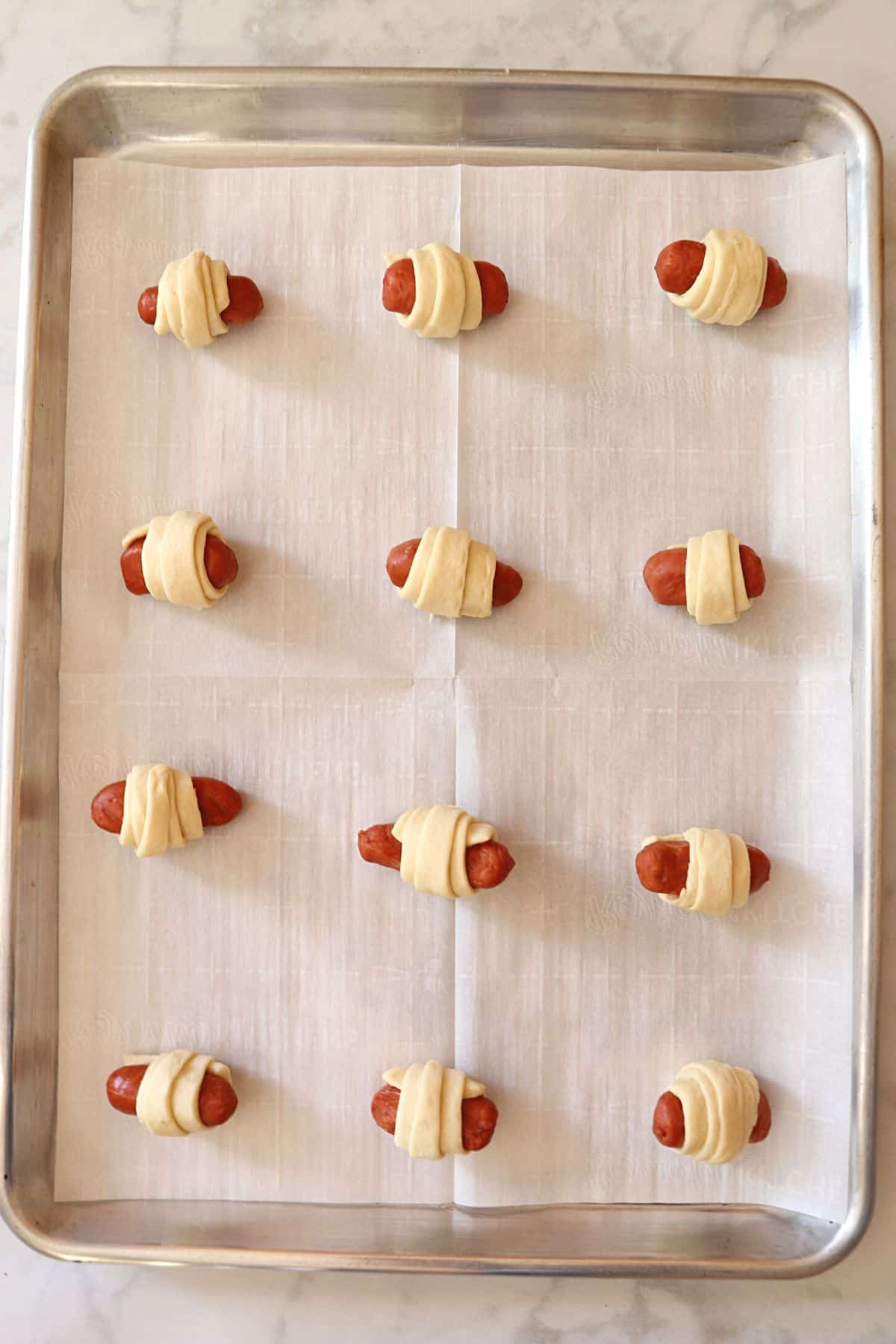 Little smokies pigs in a blanket placed on a baking sheet.