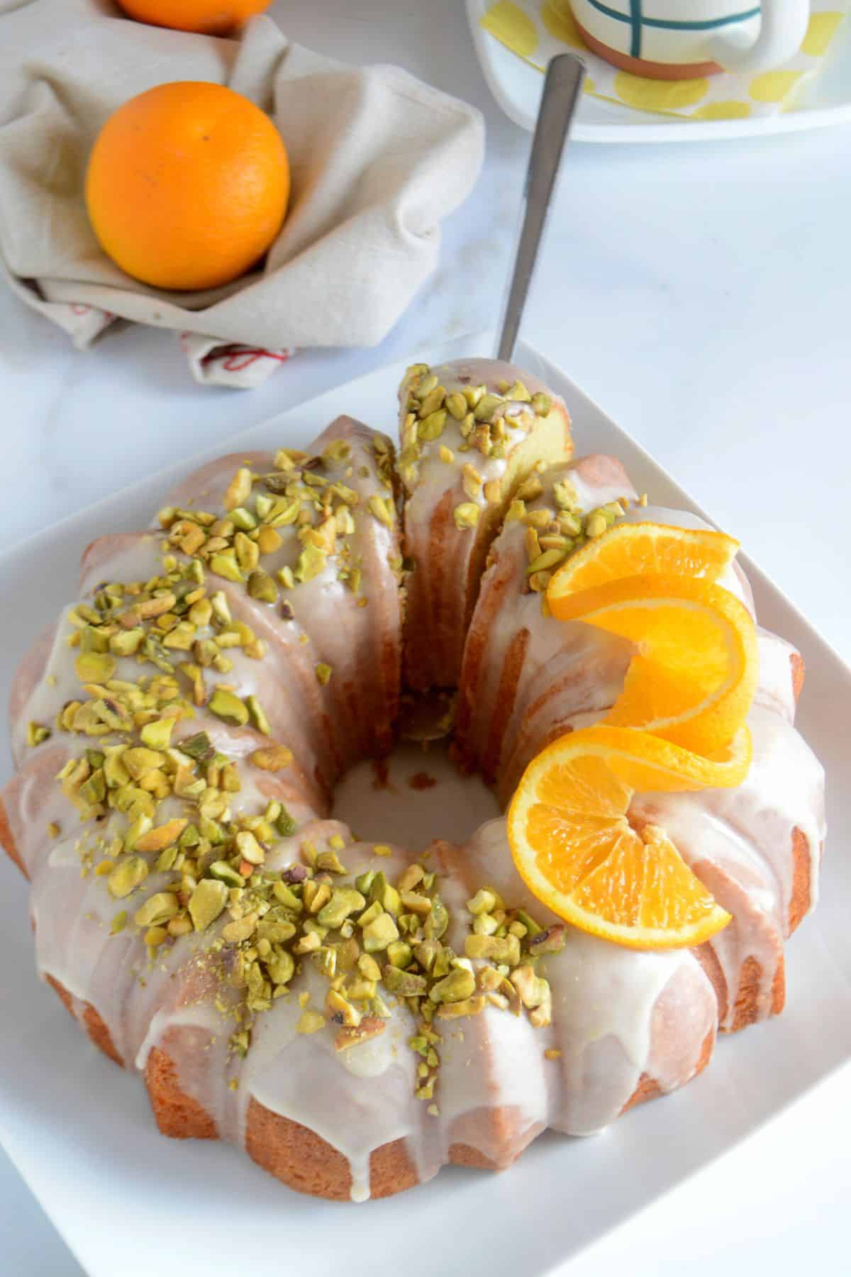 Orange bundt cake on a white platter with a piece cut from it.