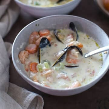 A bowl with seafood soup and a spoon in it.