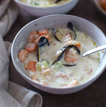 A bowl with seafood soup and a spoon in it.