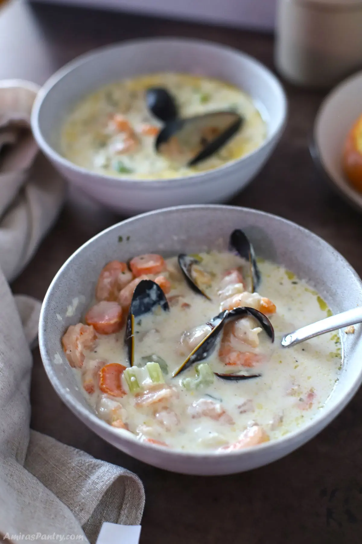 Two bowls of creamy seafood soup on a dark surface.