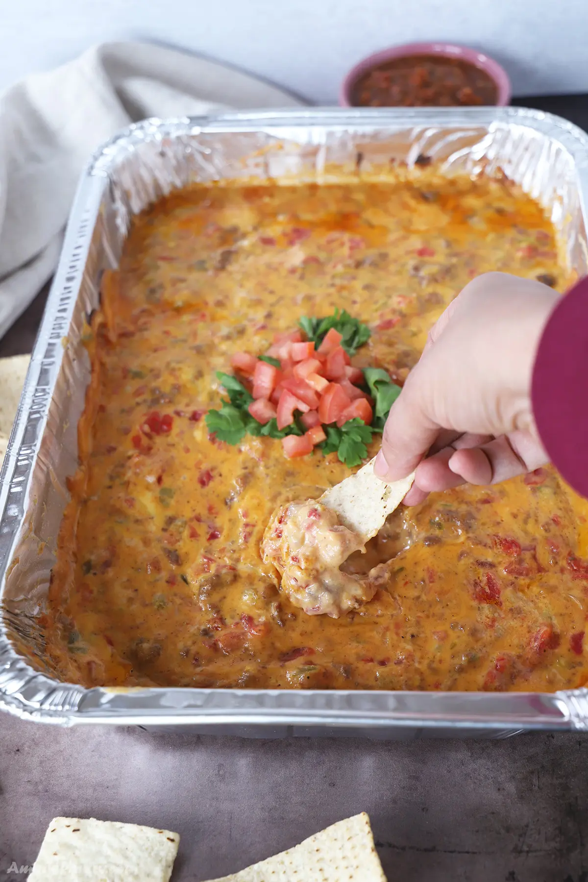 A hand scooping some smoked queso dip with tortilla chips.