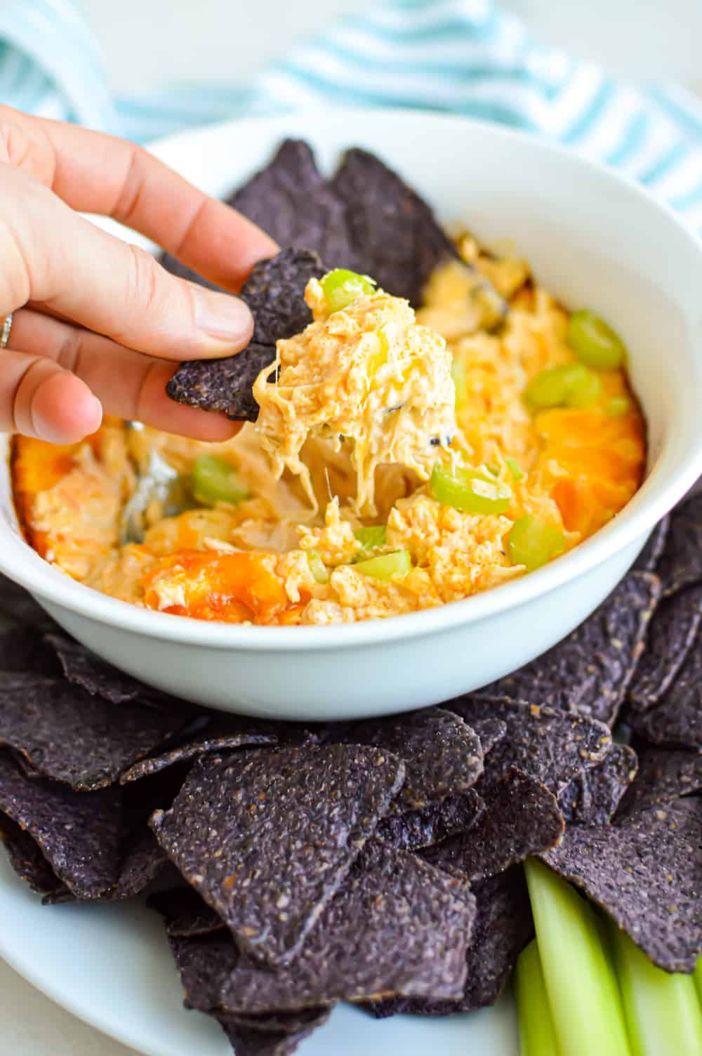 A hand with tortilla chip scooping some buffalo chicken dip out of a bowl.