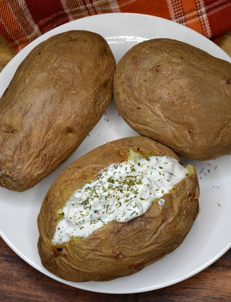 Baked potatoes on a white serving platter with one cut in half and stuffed.
