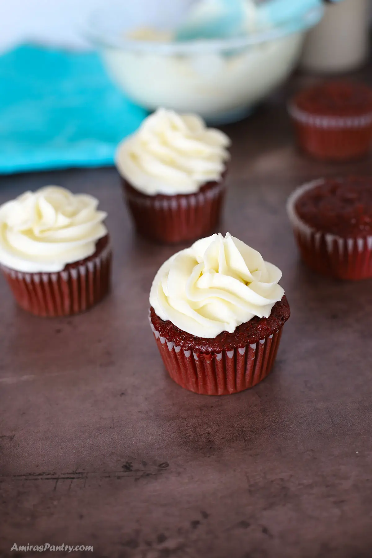 Red velvet cupcakes on a dark surface frosted with cream cheese frosting.