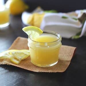 Lemon curd in a small jar with lemon wedges.