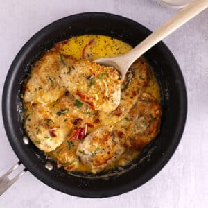 A skillet with chicken in creamy sauce with a wooden spoon in it.