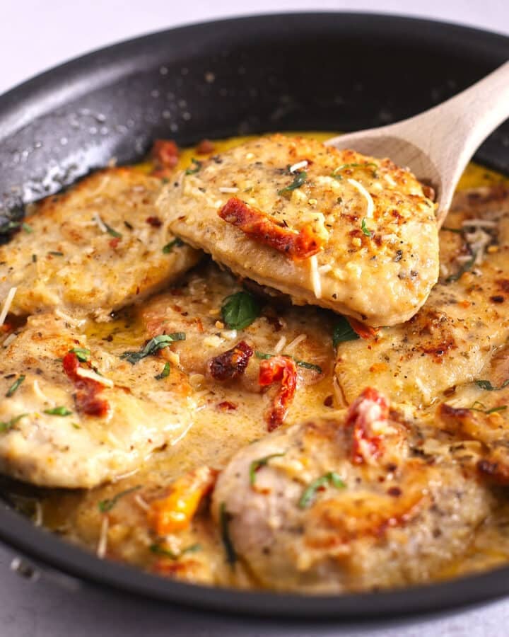 A wooden spoon scooping some chicken out of the casserole.