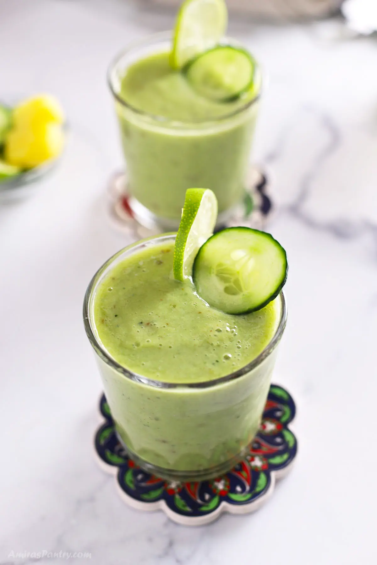 A top view shot of two green smoothie glasses with cucumber and lemon slices.