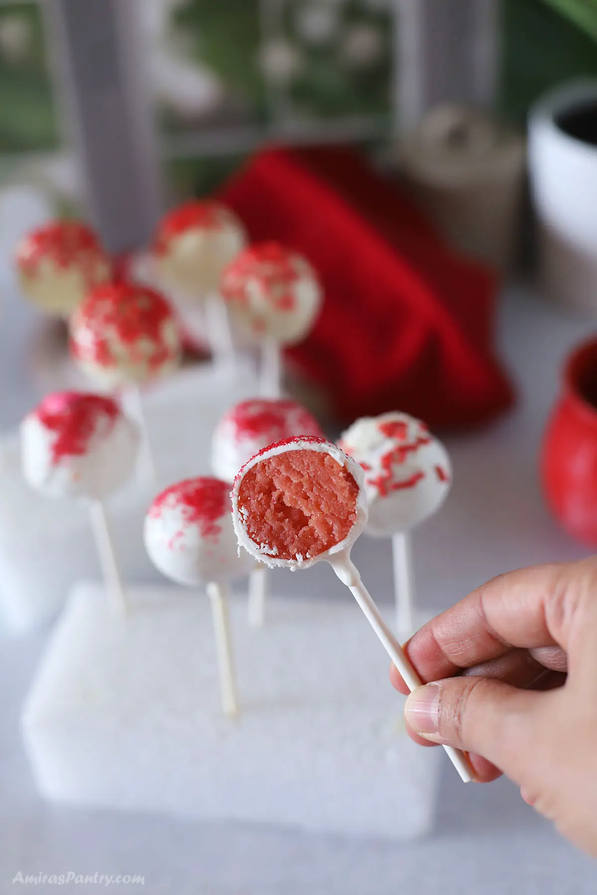 A hand holding one strawberry cake pops cut to show texture.