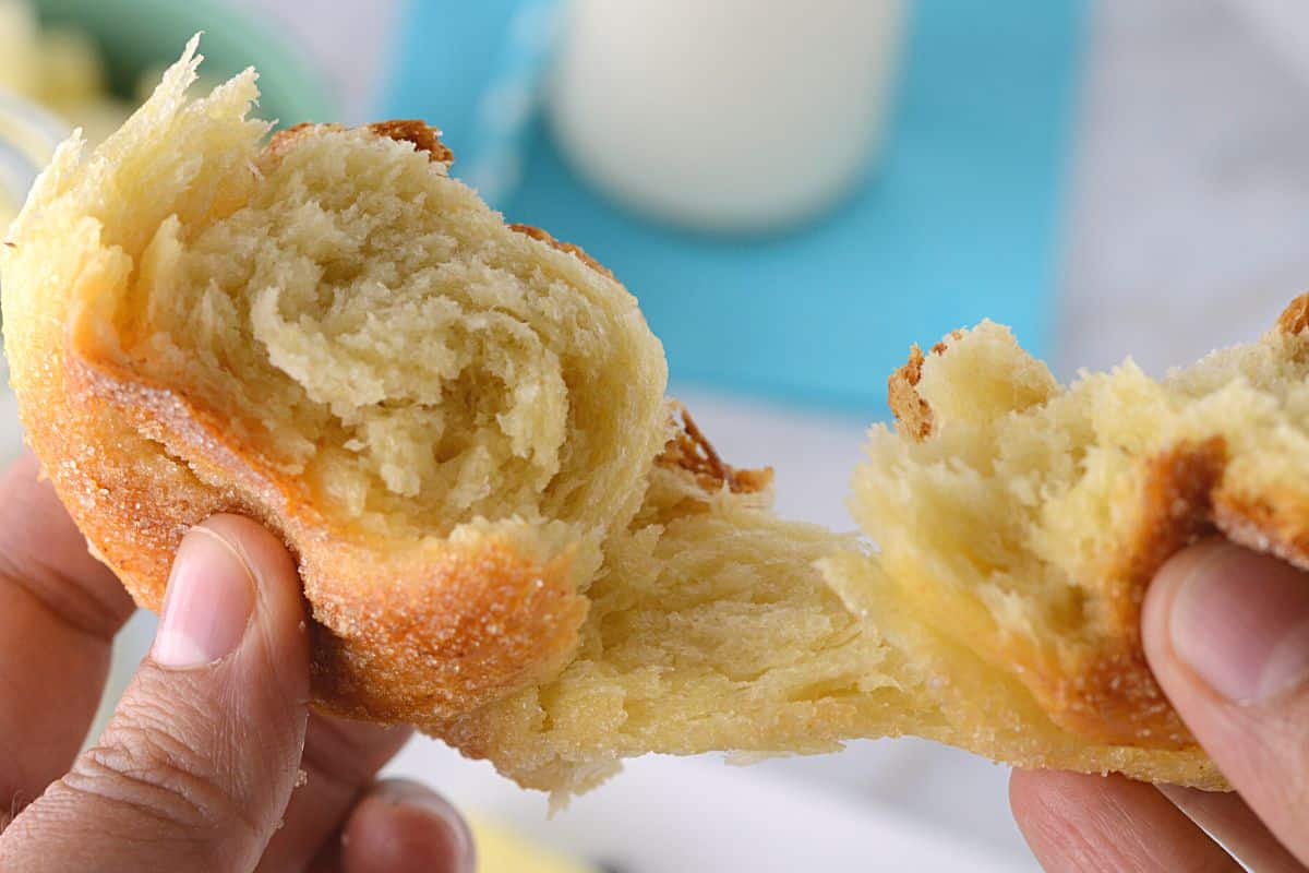 A hand cutting one sweet roll to show texture.