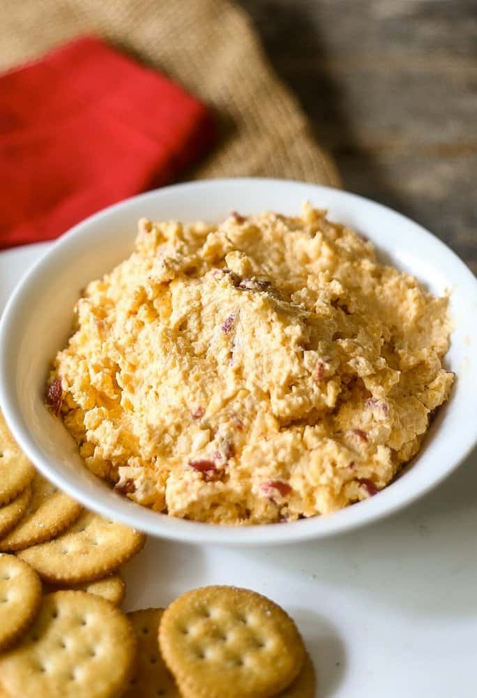 Cheese dip on a white bowl with crackers on the side.