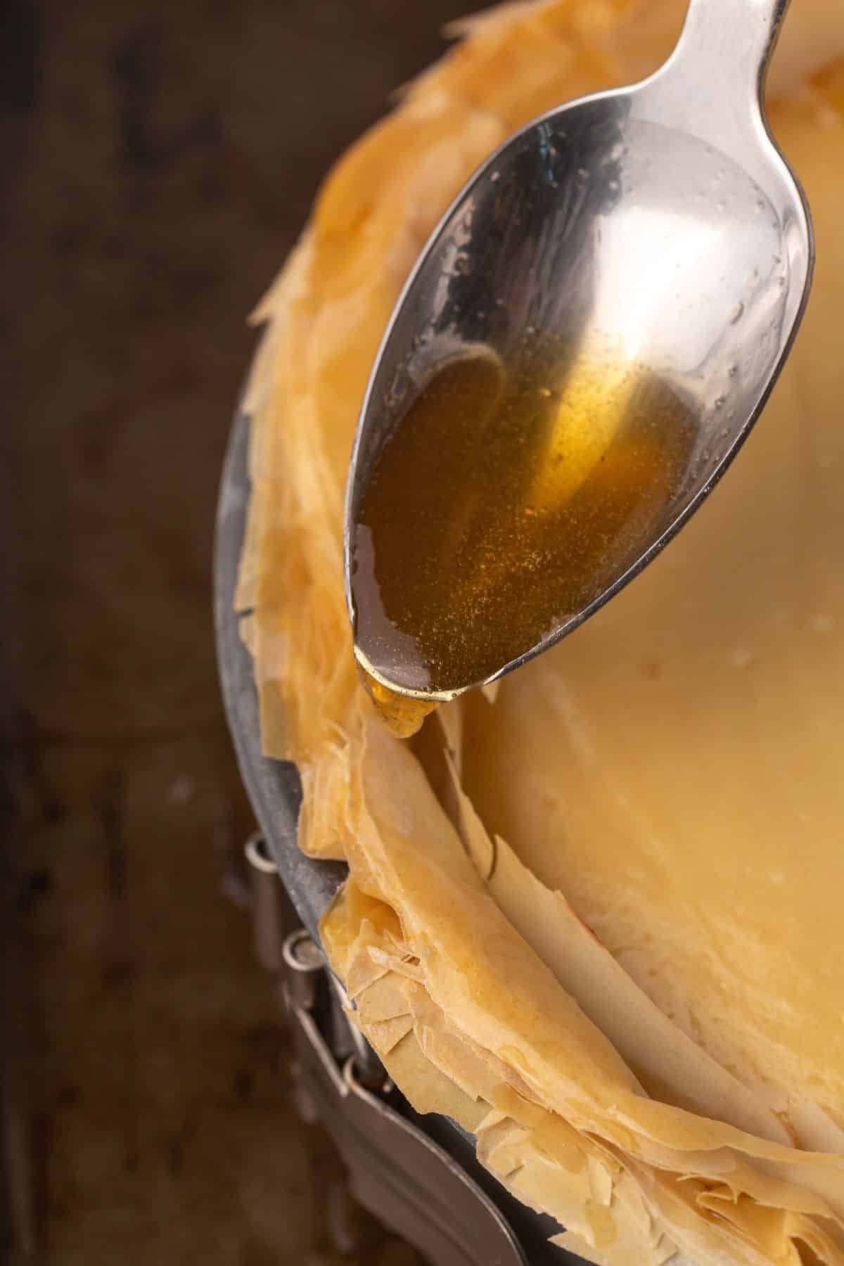 A spoon pouring some syrup over the edges of baklava cheesecake.
