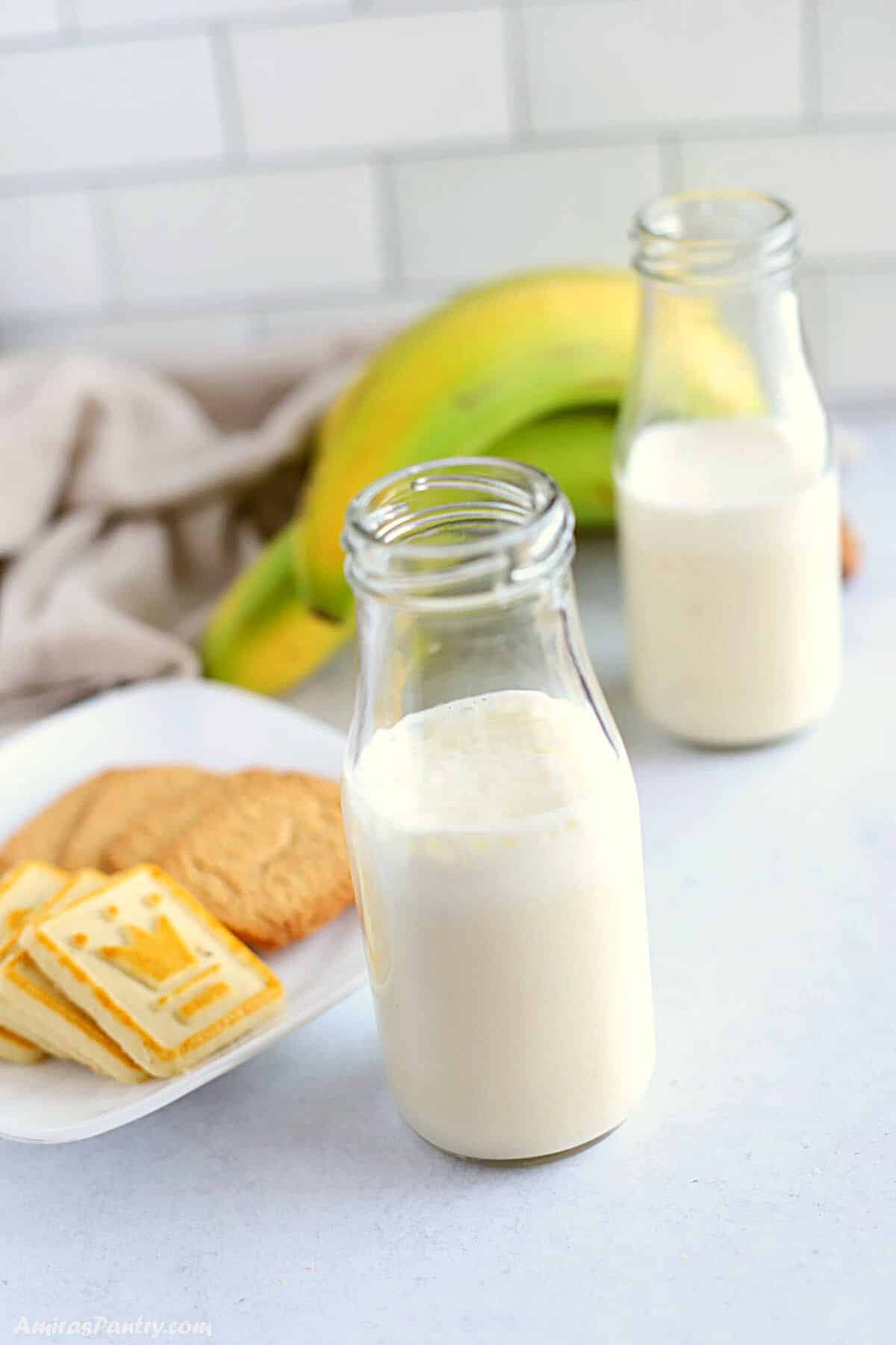 bottles of banana milk with cookies on the side and bananas on the background.