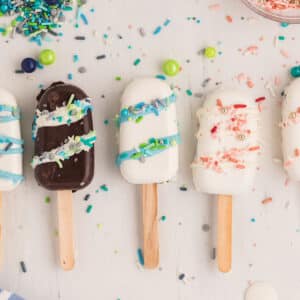 Cakesicles on a white surface with sprinkles scattered on it.