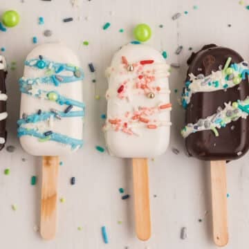 Cakesicles on a wooden surface with scattered sprinkles.