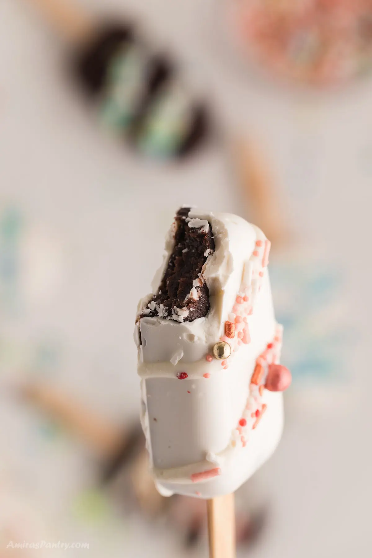 One cake popsicle covered in white chocolate with a bite taken to show texture.