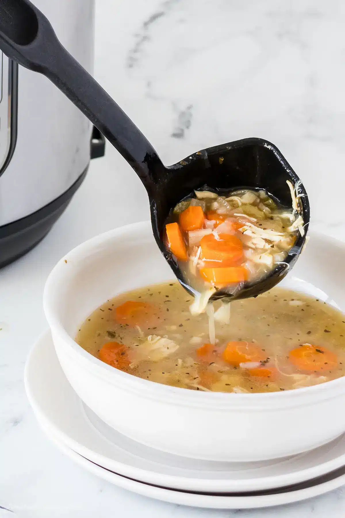 A ladle with chicken soup pouring into a serving bowl.