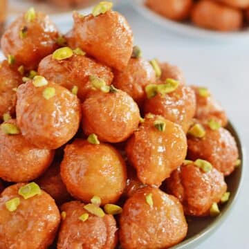 A side view of a plate with a pile of lokma balls garnished with pistachios.