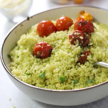 A bowl of pesto couscous garnished with fresh basil and grape tomatoes.