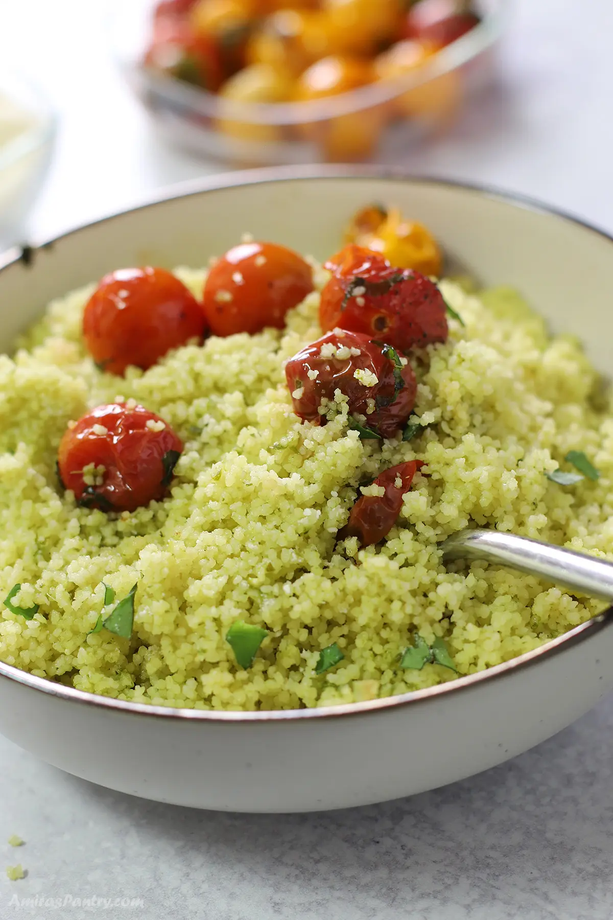 A close up look at a bowl of pesto couscous topped with cherry tomatoes.