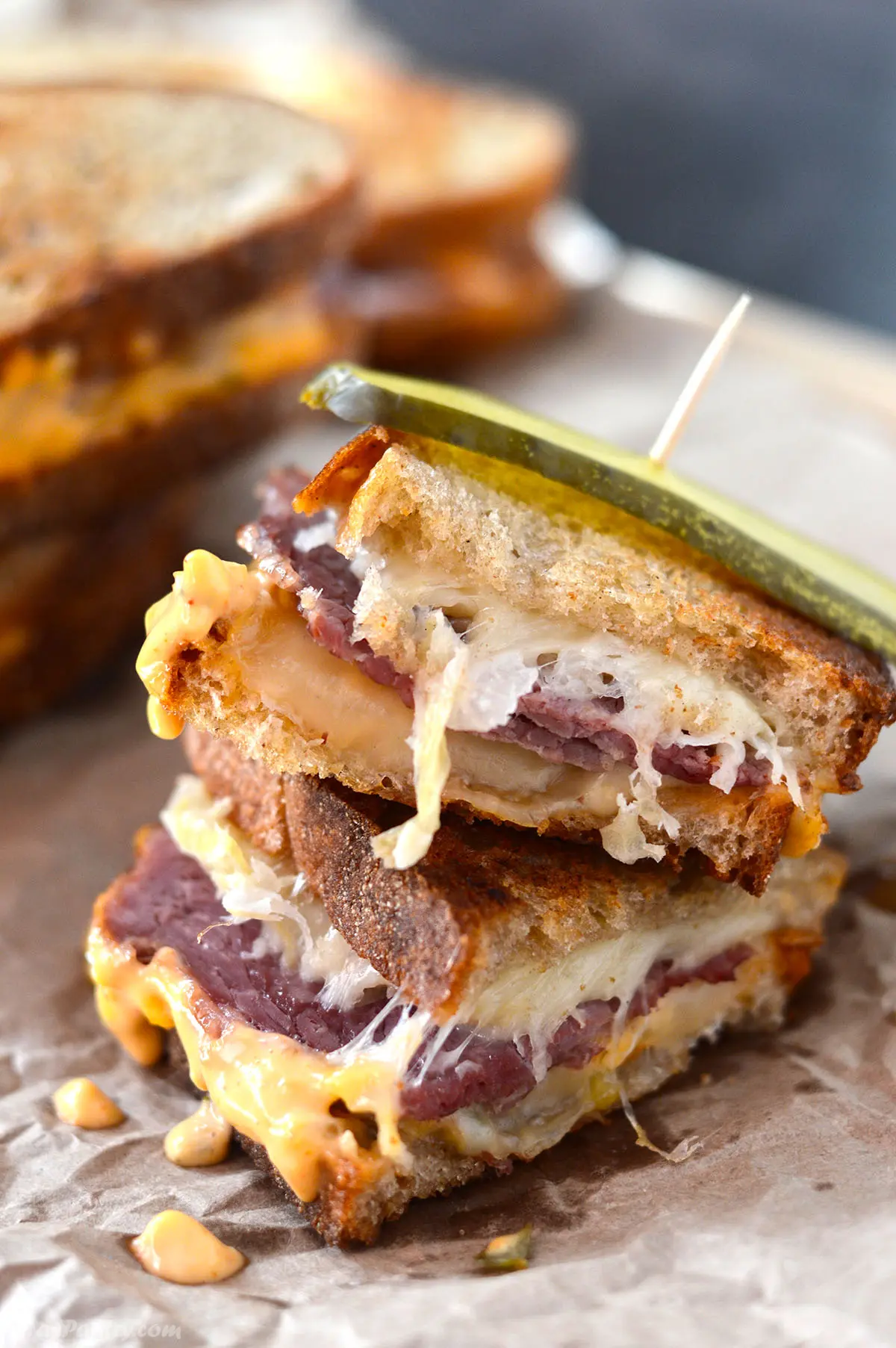 A stack of reuben sandwiches on a brown paper.