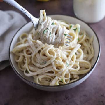 A fork with some tahini pasta over a dish of pasta.