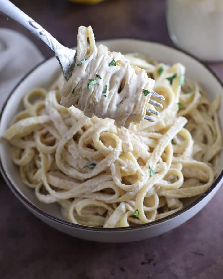 A fork with some tahini pasta over a dish of pasta.