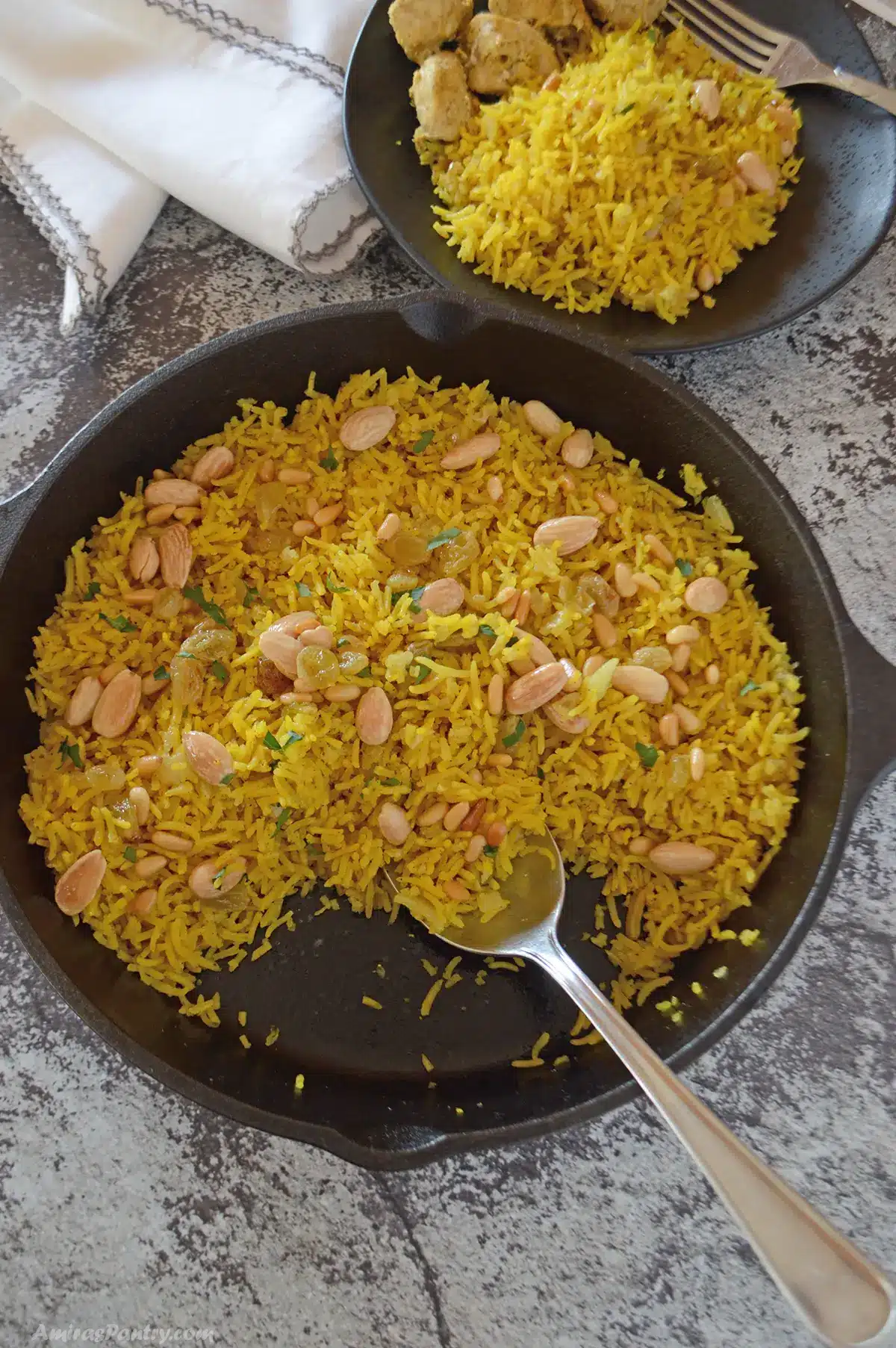 An overhead view of a skillet with yellow rice and a serving plate on the side.