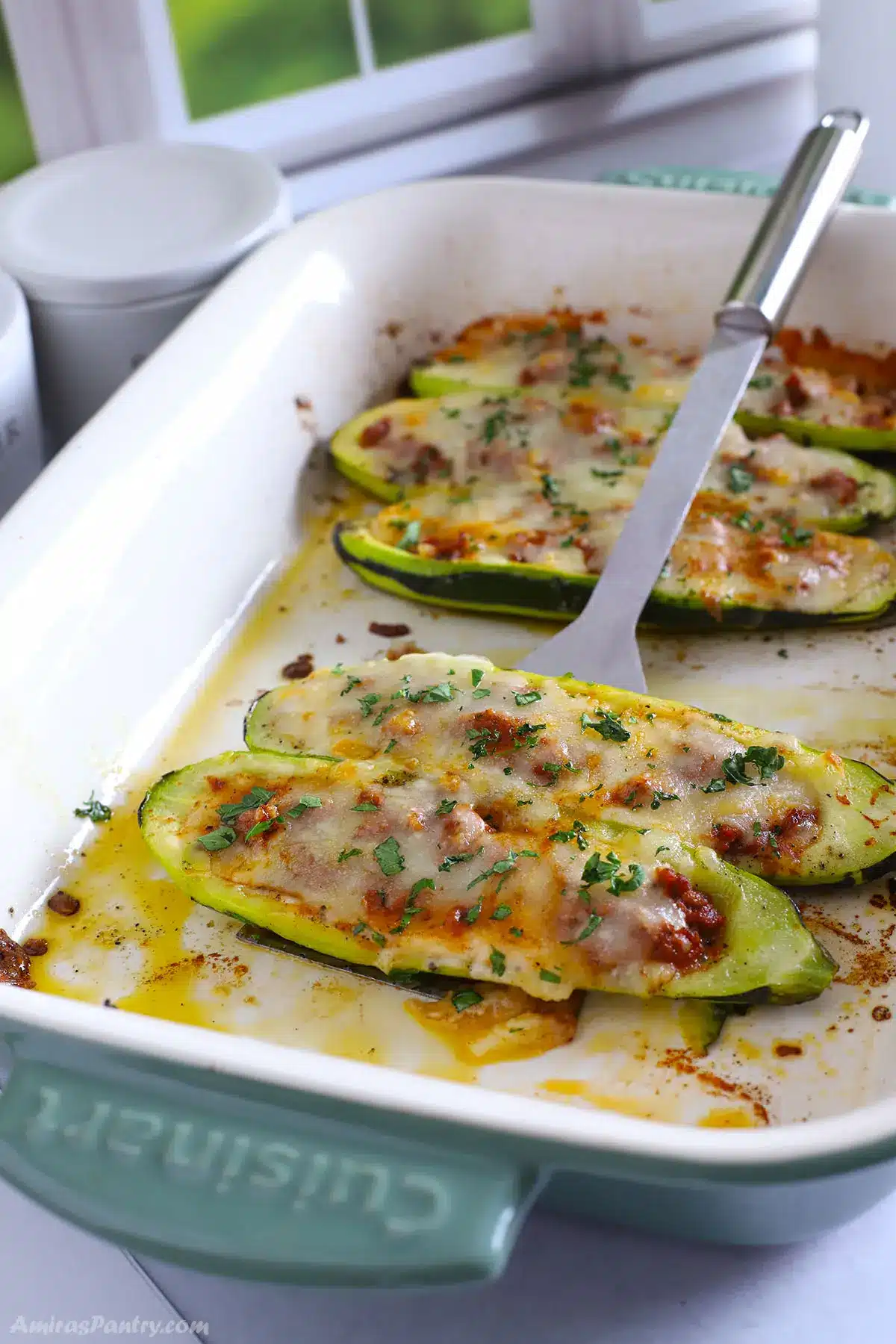 A serving spoon with zucchini boates being lifted from the casserole.