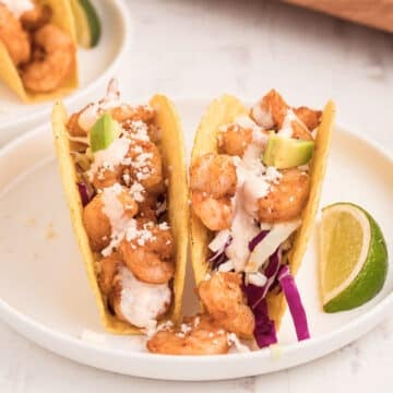 A dinner plate with two shrimp tacos with lemon wedges.