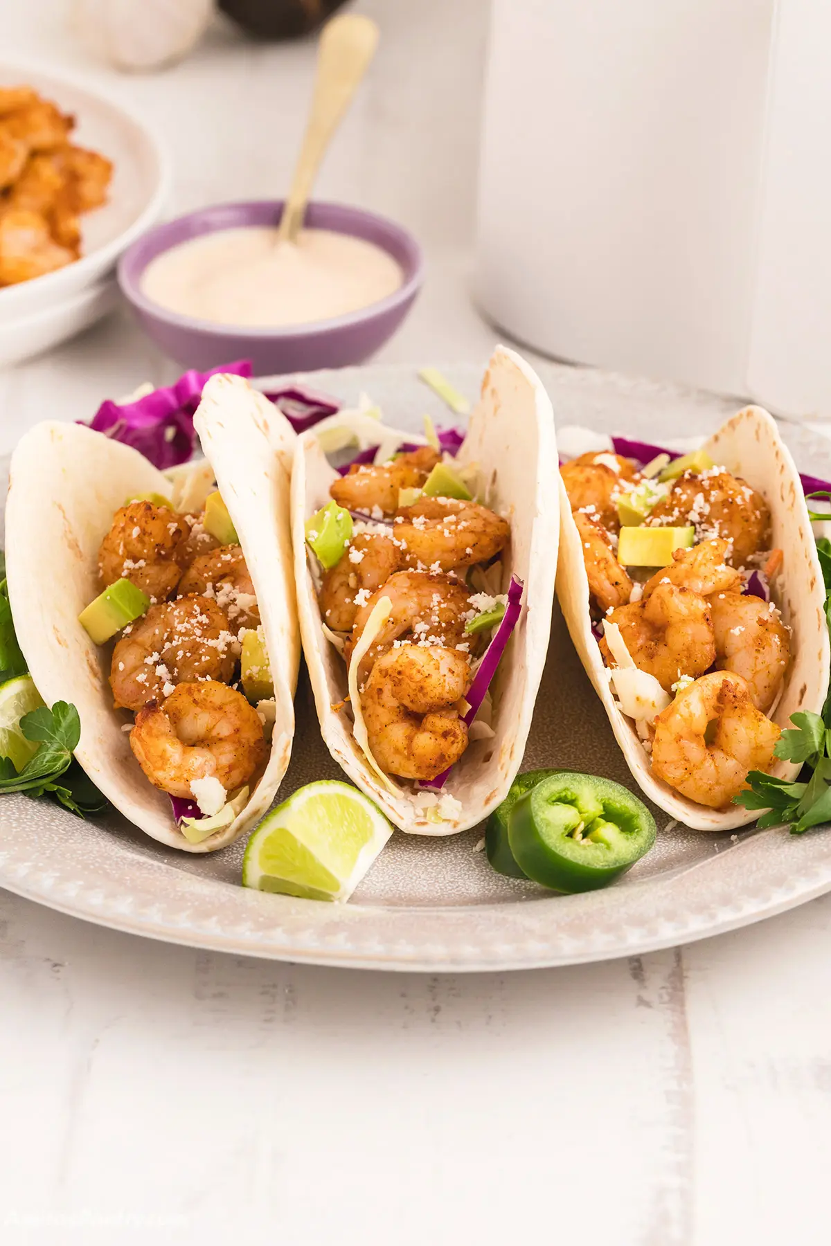 Three shrimp tacos on a serving platter with sauce.