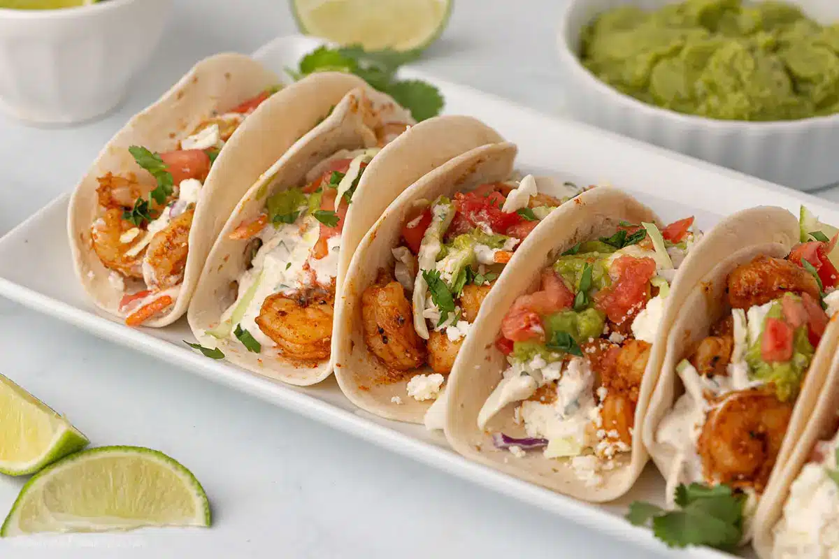 A big rectangular white platter with shrimp tacos and guacamole on the side.