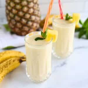 Two tall glasses of banana pineapple smoothie.