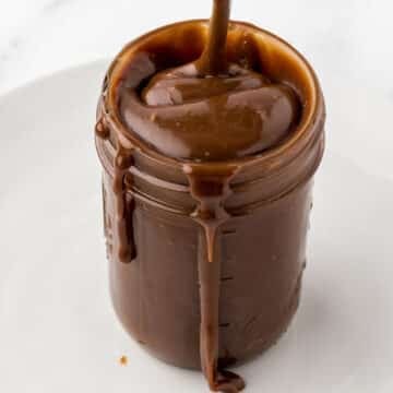 A jar with hot fudge sauce overflowing.
