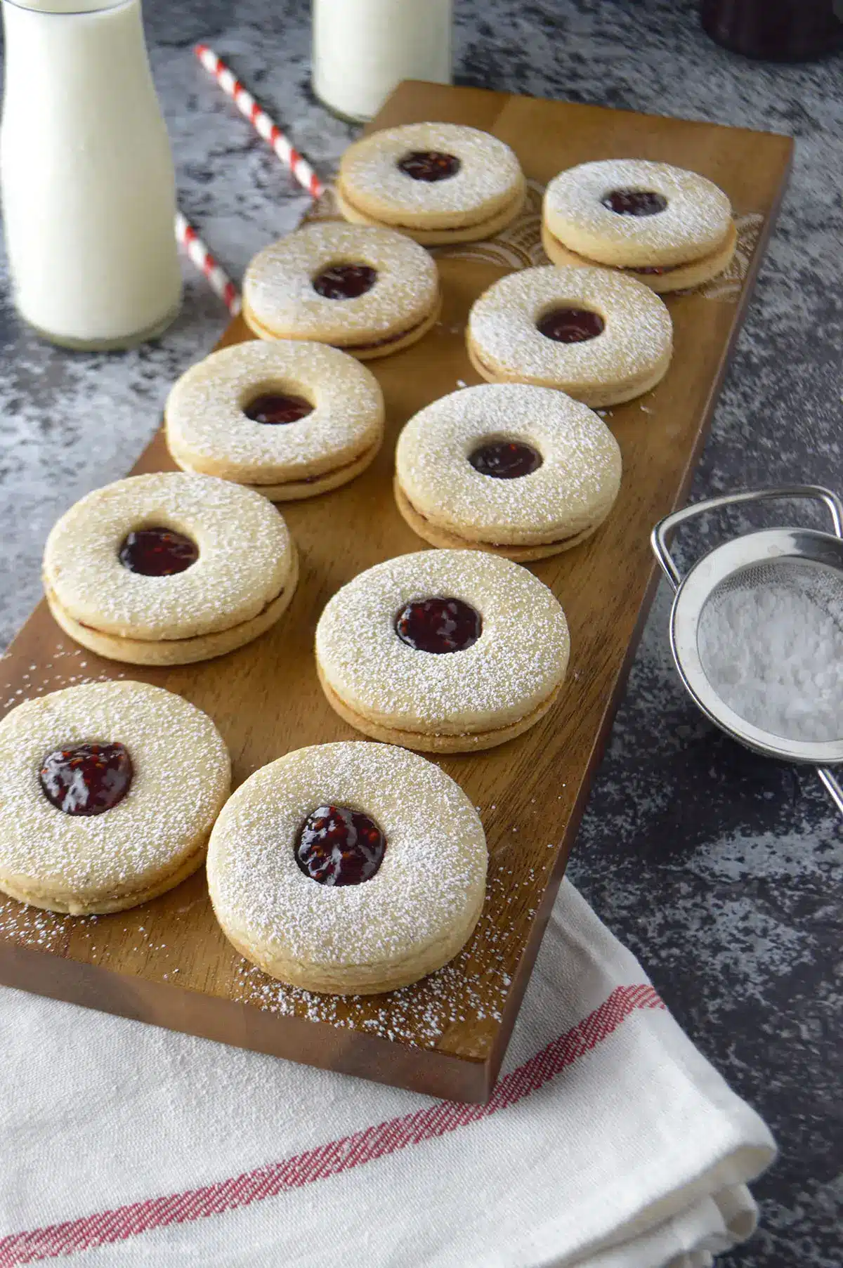 Linzer cookies filled with raspberry jam and placed on a wooden board.