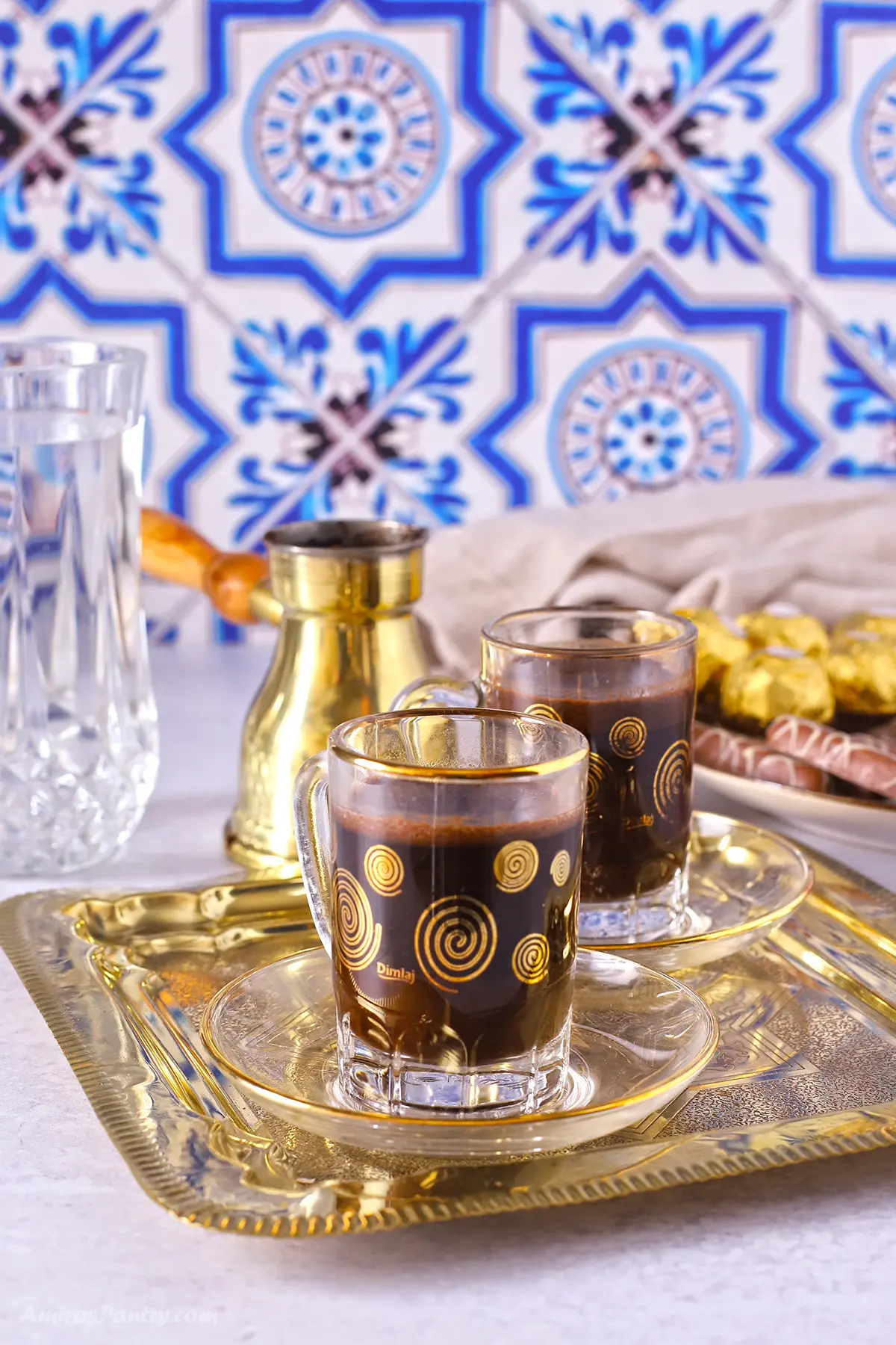 A tray with two Turkish coffee cups, a tall glass of water and some candy on the side.