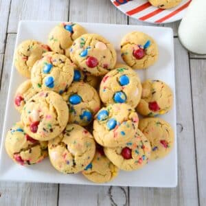 A white serving plate with m&m cookies and milk on the side.
