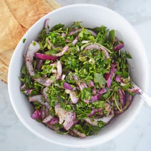 A white serving bowl with arugula salad with some pita bread on the side.